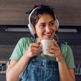 young woman sipping coffee and listening to headphones in her kitchen