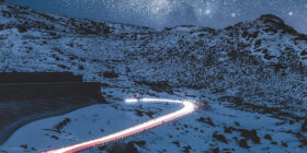Night time landscape showing a snowing mountain and a road with car lights on it