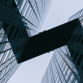 Looking straight up between 2 tall buildings with a bridge between the 2 buildings