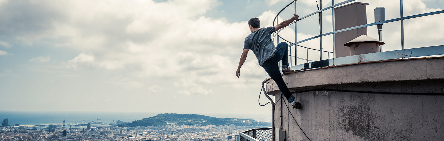 Man practicing parkour and hanging from the side of tall structure looking out at the city